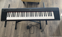 Top view of Yamaha digital keyboard piano on a black metal stand with sustain pedal beneath the keyboard.