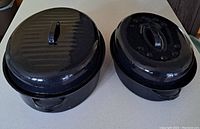Two black enamel roasting pans with lids, viewed from above showing lids on.