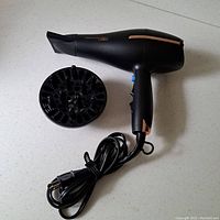 Black Conair hair dryer with concentrator nozzle lying flat and diffuser attachment beside it on white surface.