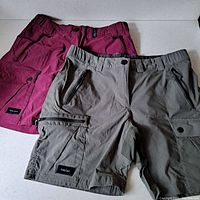 Two pairs of women's cargo shorts from Decathlon in gray and burgundy color showing front and pockets with Forclaz branding.