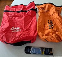 Two Foamline dry sacs (red and orange) placed on a surface with a Foamline dry sac liner in unopened packaging in front.
