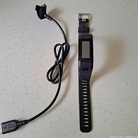 Top view of Garmin Vivosmart fitness tracker watch with attached black silicone band and charging cable beside it on a light surface.