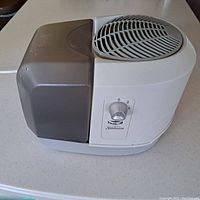 Side front view of the white and gray Sunbeam humidifier showing control knob and vent.