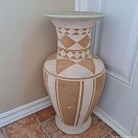 Image showing large decorative vase with geometric beige and white pattern, placed in corner against wall and door.