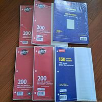Photo showing four packages of Hilroy lined paper with red covers and 200 sheets each, plus two packages of refill lined paper with 150 sheets each (Staples and blue cover). All are sealed.