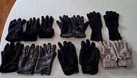 Top view of various pairs of gloves and mittens arranged on a table, showing different materials including leather and knit fabric.