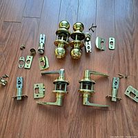 Brass door handles and components organized on wooden floor.
