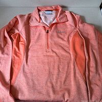 Coral orange heathered Columbia pullover laid flat showing front with quarter zip collar and embroidery.