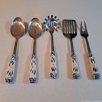 Five serving utensils arranged in a row on a countertop showing stainless steel heads and blue and white patterned handles.