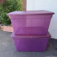 Photo showing two stacked purple Sterilite storage containers with lids outdoors on asphalt with some greenery in background