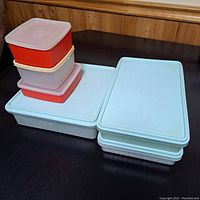 Photo showing 8 Tupperware plastic food storage containers with lids in various sizes and colors including red, pink, and white.
