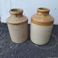 Two vintage stoneware crocks with earthy glazing, cylindrical shape and wide lips shown from front view.