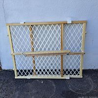 Wooden safety gate laying against wall showing front side with adjustable width and mesh design, with ruler for scale.