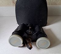 Front view of Yashica binoculars with lens caps on and leather carrying case in background.