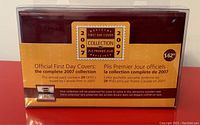 Full front view of the wooden case packaging showing the label describing the contents as the 2007 Official First Day Covers Collection containing 29 items, sealed condition.