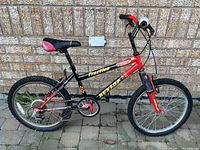 Side view of boys BMX bike showing red and black frame with Friction and Dunlop decals, 6 speed drivetrain, knobby tires, and seat.