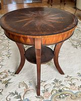 Front-facing view showing round top, starburst inlay, curved legs, and lower shelf