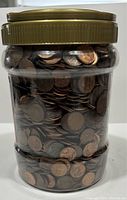 Side view of clear plastic jar filled with Canadian copper pennies, showing coin details through container.