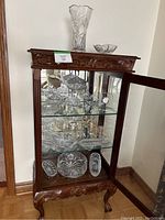 Full display cabinet with top crystal vase, bowl, and a variety of cut crystal bowls and trays visible on three glass shelves.
