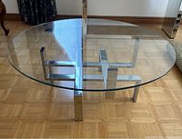 Oblique side view of the round glass top coffee table showing the chrome base and glass thickness