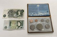 Photo showing two British one pound banknotes, visible serial numbers, and differing design styles.