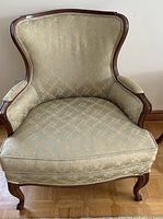 Front view of vintage Queen Anne style armchair upholstered in greenish gold damask fabric with wooden frame and carved legs.