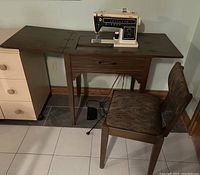 Full view of the Singer sewing machine mounted in a fold-down wooden table, with matching chair and foot pedal visible below.