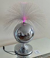 Full view of lamp showing chrome spherical base and fiber optic strands illuminated in pink.