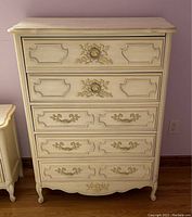 Front view of white and gold French Provincial 5 drawer tall boy dresser showing gold accents on drawer fronts and top scalloped edge.