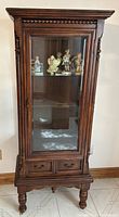 Front view of cabinet with glass door closed showing ornate wood trim and interior contents