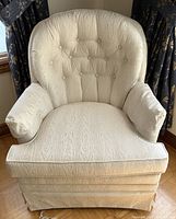 Front-facing view showing the full armchair with white fabric, button tufted back, skirted base, and removable cushion.