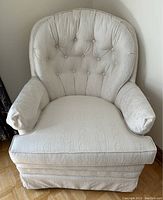 Front view of white button tufted armchair with swivel rocking base.