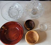 Top view showing all six bowls arranged on a surface, two clear glass with patterns and four wooden in various finishes and sizes.