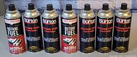 Eight butane fuel cylinders arranged linearly showing brand names Chef Master and Burton with different levels of fullness.