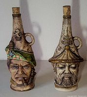 Side by side photo of the two ceramic wine bottles in the shape of male faces wearing unique hats