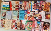 Photo showing a variety of cookbook covers stacked and spread out with titles visible and colorful food images.