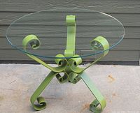 Clear view of the round glass tabletop and decorative heavy metal base with curls and scrollwork, showing color and structure.
