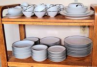 Full view of china set on wooden rack showing teacups, saucers, plates of various sizes, creamer and gravy boat.