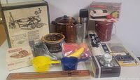 Full view of the kitchen lot items arranged on a surface including frame, sharpener, cups, thermos, shakers, scoops, and boxed items