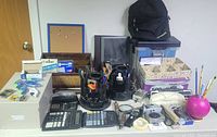 Front view of office supplies showing wooden organizer, calculators, tape dispensers, cork board, pens, staplers, and other various office supplies