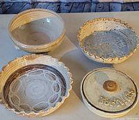 Four handmade pottery items displayed on a table: two scalloped edge bowls with patterned interiors, one plain bowl, and one covered tortillas holder with inscription on lid.