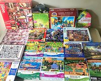 Overview photo of various boxed jigsaw puzzles arranged on a flat surface, showing multiple brands and piece counts.