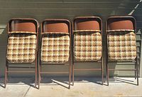 Front view of four brown Samsonite folding chairs with padded checkered seat cushions arranged in a row.