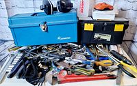 Photo showing the assortment of tools spread out with two toolboxes (blue metal Companion and black plastic with yellow latches), ear protection earmuffs on top, and various hand tools such as pipe wrench, pliers, cutters, and wrenches.