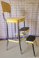 Full view of vintage Cosco Stylaire chair step stool showing yellow padded backrest, seat and chrome frame with two steps.