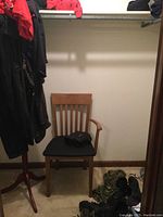 Wooden chair with black cushioned seat and broken armrest beneath an empty clothes rack, various boots on floor