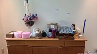 Overview of lot items on wooden cabinet including heart-shaped candles, brass lantern, trays, vase with potpourri, drying rack, and box.