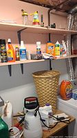 Shelf with assorted cleaning supplies including stain removers, bleach, insect control, and detergent containers with wicker wastebasket below