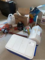 Overview of lot showing coolers, hedge trimmer, tools, potting soil, boxes and other items scattered on floor.