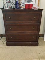 Front view of the wooden dresser with three drawers, brass handles, and visible scratches